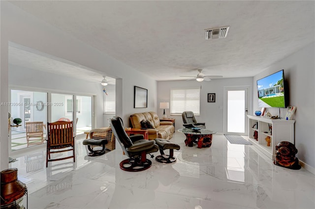 living area featuring visible vents, baseboards, a ceiling fan, marble finish floor, and a textured ceiling