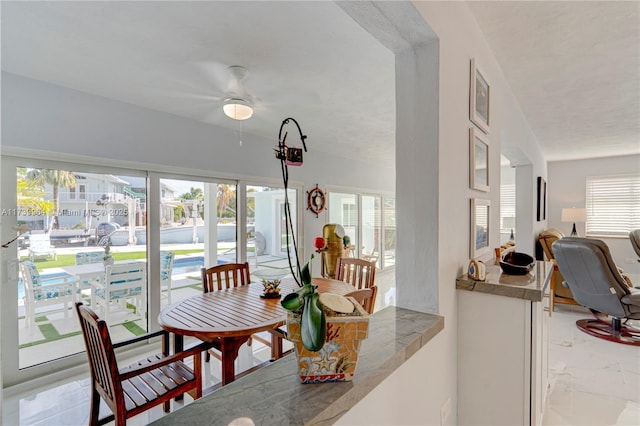 dining space with a ceiling fan, marble finish floor, and plenty of natural light