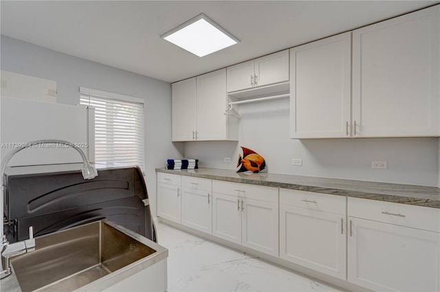 kitchen with dark countertops, marble finish floor, fridge, and white cabinets