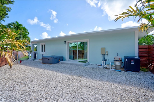 rear view of house featuring a patio area, a hot tub, fence, and stucco siding