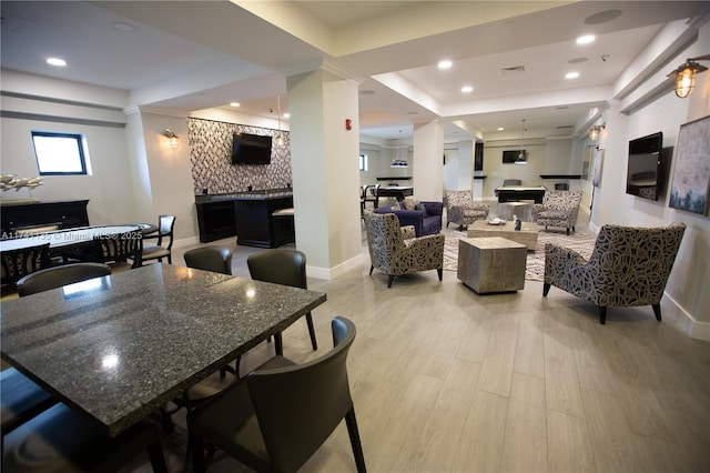 dining area featuring decorative columns, a raised ceiling, and light wood-type flooring