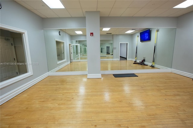 workout room featuring a paneled ceiling and light wood-type flooring