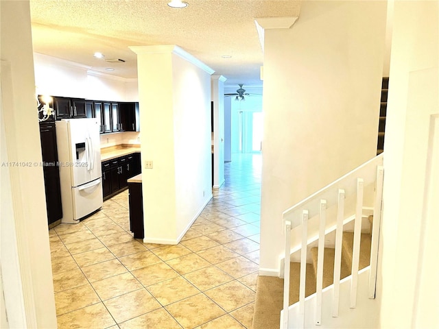 kitchen featuring light tile patterned flooring, white refrigerator with ice dispenser, ceiling fan, crown molding, and a textured ceiling