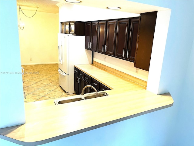 kitchen featuring light tile patterned flooring, dark brown cabinetry, sink, and white fridge