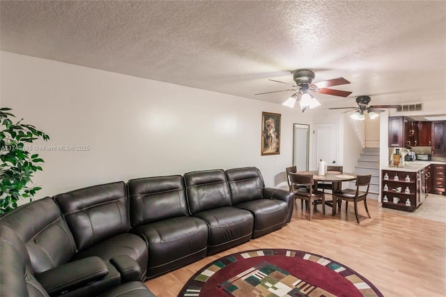 living room with ceiling fan, light hardwood / wood-style floors, and a textured ceiling