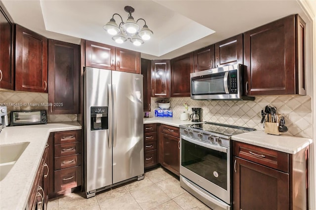 kitchen featuring light tile patterned flooring, appliances with stainless steel finishes, tasteful backsplash, a tray ceiling, and light stone countertops