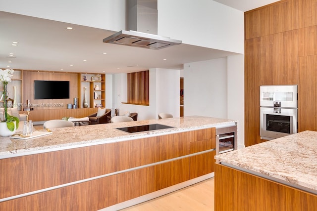 kitchen with light stone counters, light hardwood / wood-style flooring, black electric cooktop, a fireplace, and range hood