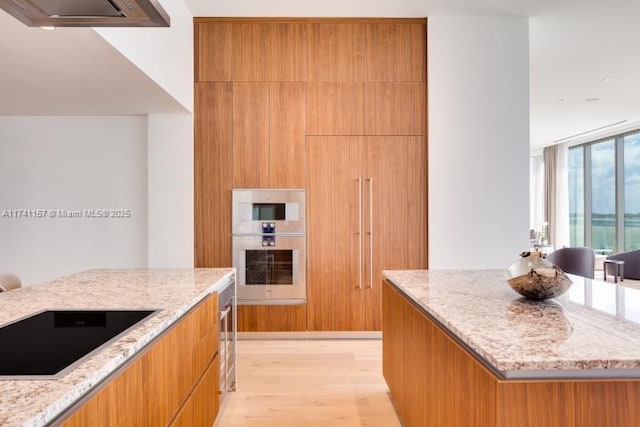 kitchen with black electric stovetop, light stone countertops, and light wood-type flooring