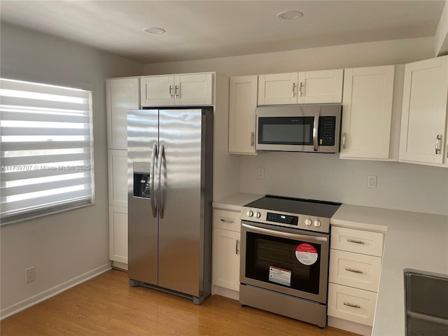 kitchen with stainless steel appliances, white cabinetry, and light hardwood / wood-style floors