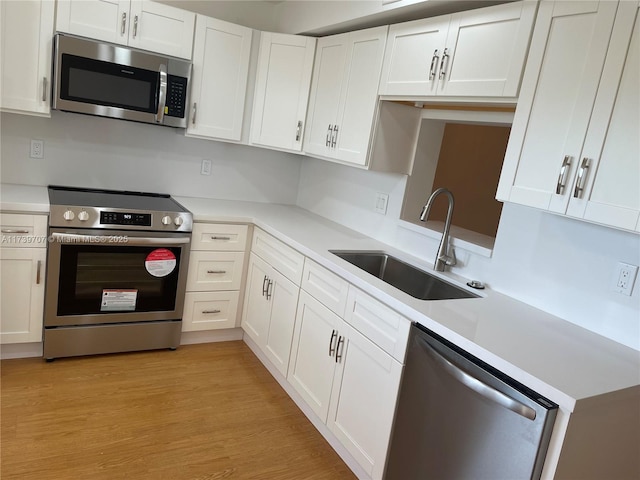 kitchen with light wood-type flooring, stainless steel appliances, sink, and white cabinets