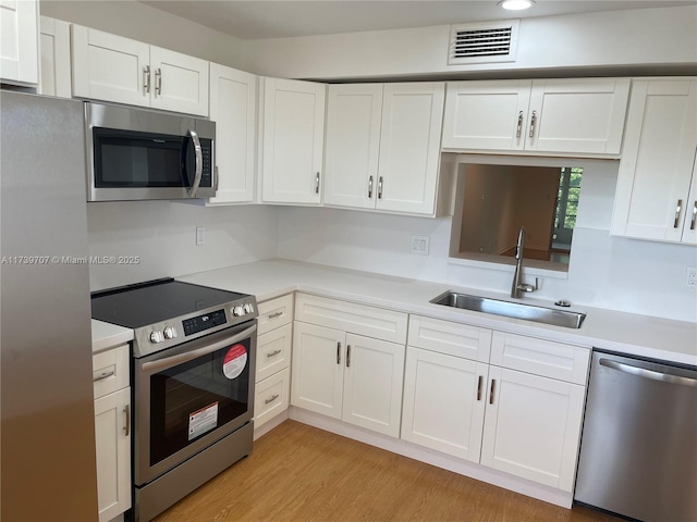 kitchen with stainless steel appliances, white cabinetry, sink, and light hardwood / wood-style flooring