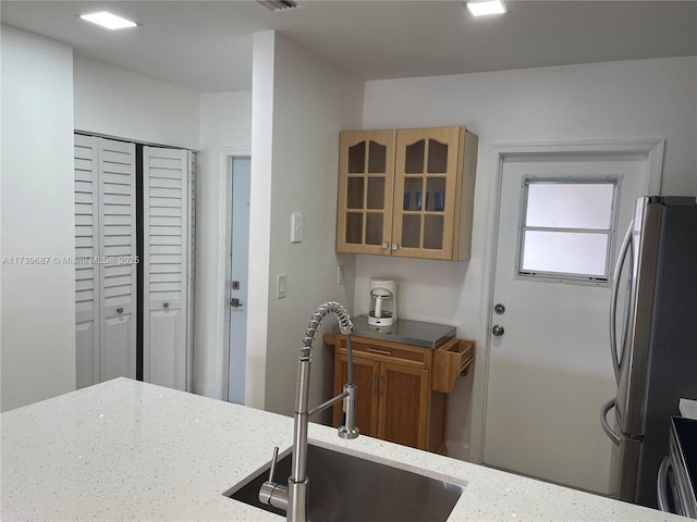 kitchen featuring light stone counters, stainless steel fridge, sink, and stove