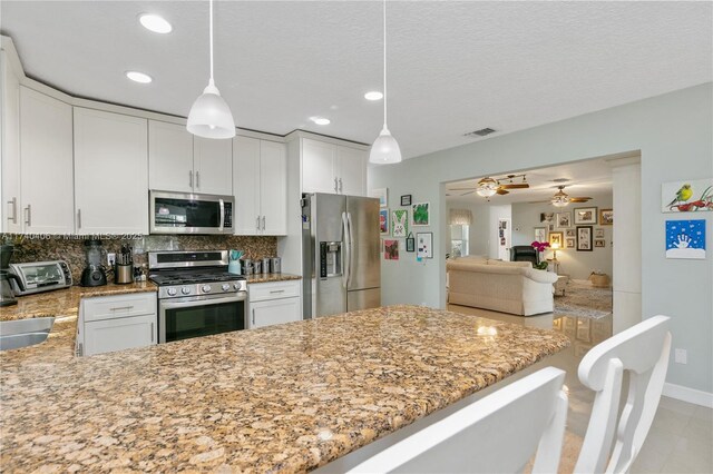 kitchen with pendant lighting, white cabinetry, light stone countertops, and appliances with stainless steel finishes