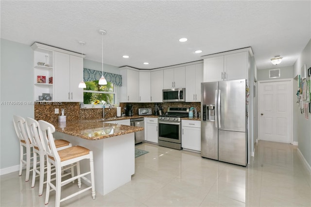 kitchen with stainless steel appliances, decorative backsplash, white cabinets, a sink, and a peninsula