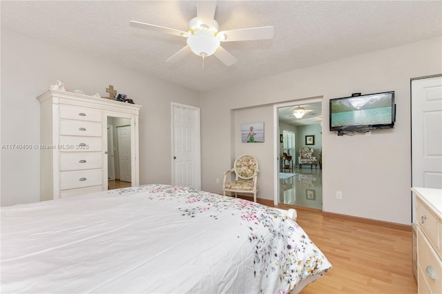 bedroom featuring light wood finished floors, ceiling fan, baseboards, and a textured ceiling