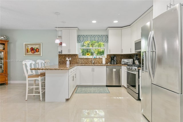 kitchen featuring a breakfast bar area, appliances with stainless steel finishes, stone countertops, decorative light fixtures, and kitchen peninsula