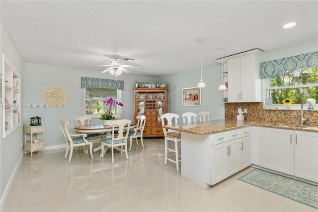 kitchen with decorative backsplash, white cabinetry, a sink, light stone countertops, and a peninsula