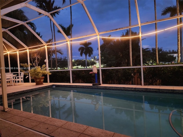 pool at dusk with a lanai and a patio area