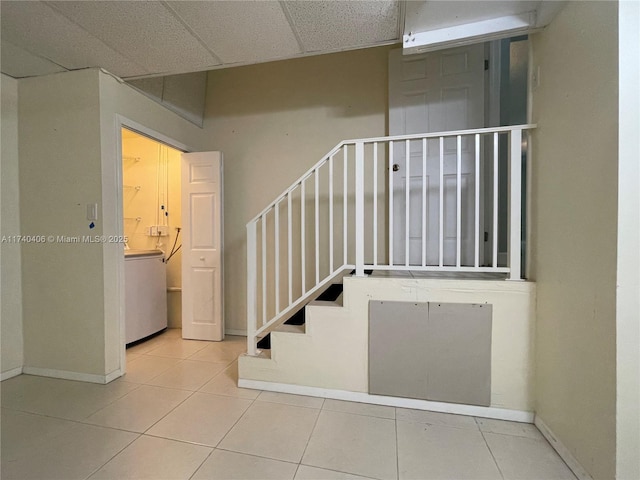 staircase featuring a paneled ceiling, washer / dryer, tile patterned flooring, and baseboards