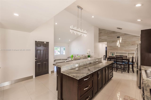 kitchen featuring stainless steel refrigerator, decorative light fixtures, light tile patterned floors, light stone counters, and dark brown cabinets