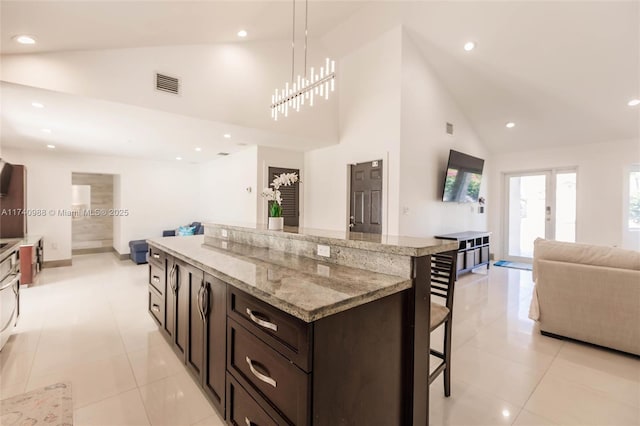 kitchen with a kitchen bar, dark brown cabinets, light stone counters, a kitchen island, and decorative light fixtures