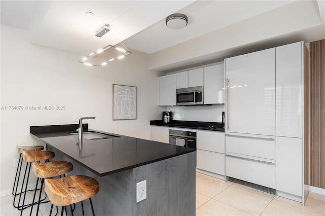 kitchen featuring sink, white cabinetry, hanging light fixtures, a kitchen breakfast bar, and oven