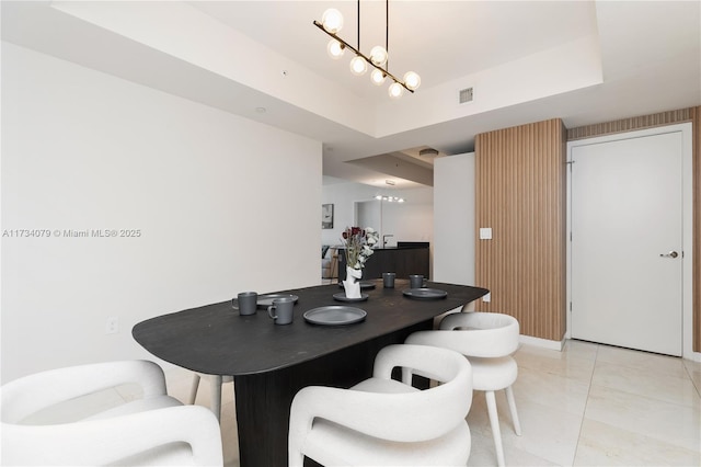 tiled dining area with a raised ceiling and a chandelier