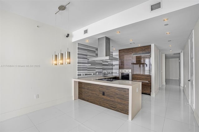 kitchen with island exhaust hood, stainless steel oven, light tile patterned floors, and decorative light fixtures