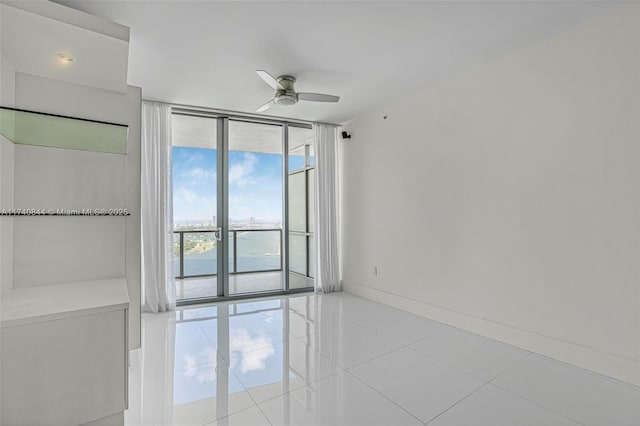 empty room featuring ceiling fan, a water view, light tile patterned floors, and a wall of windows