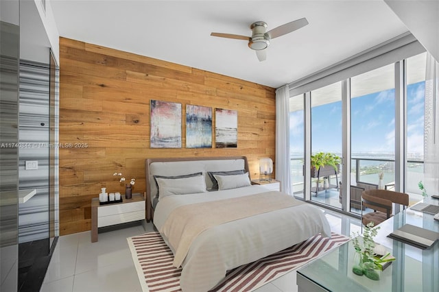 bedroom with ceiling fan, wooden walls, a water view, expansive windows, and access to outside