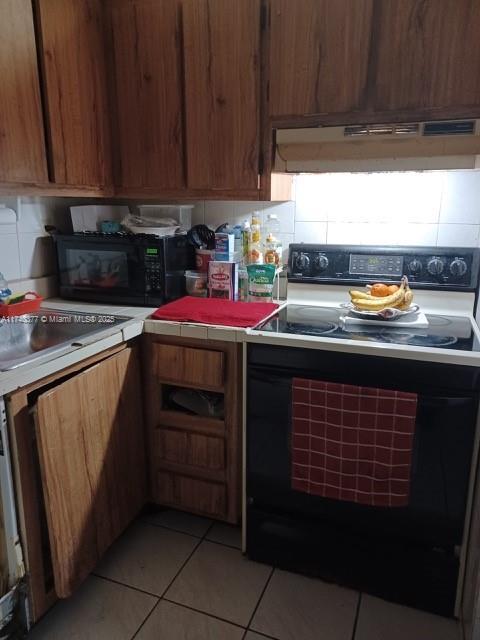 kitchen featuring light tile patterned floors, backsplash, black appliances, and sink