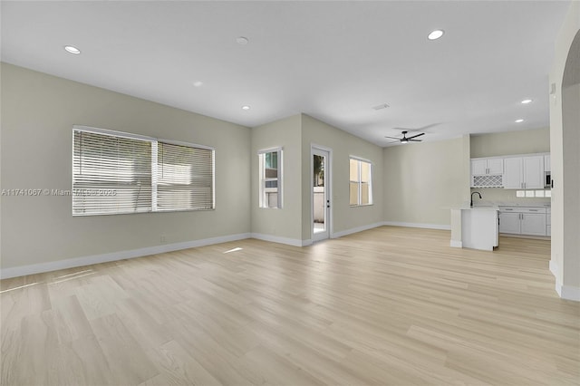 unfurnished living room with sink, light hardwood / wood-style floors, and ceiling fan