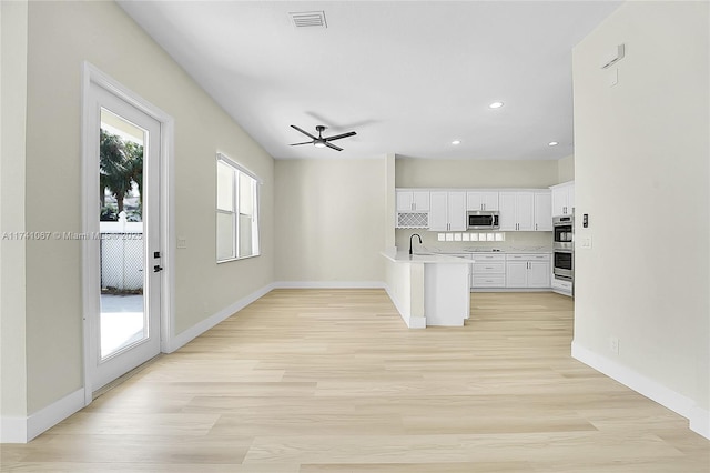 kitchen with stainless steel appliances, sink, white cabinets, and light hardwood / wood-style flooring