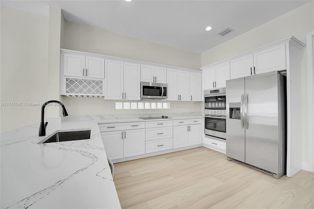 kitchen with appliances with stainless steel finishes, sink, white cabinets, light stone counters, and light wood-type flooring