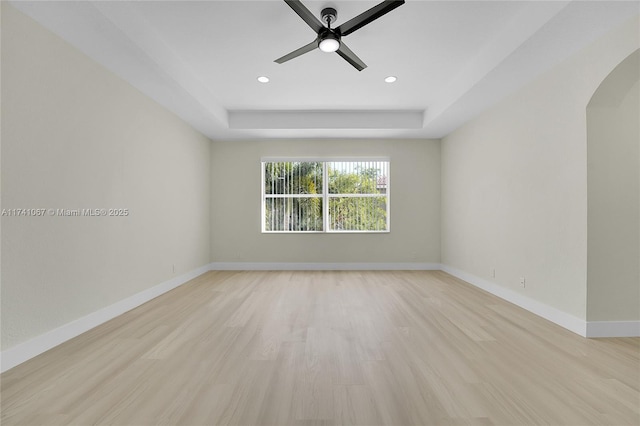 unfurnished room with light hardwood / wood-style flooring, ceiling fan, and a tray ceiling