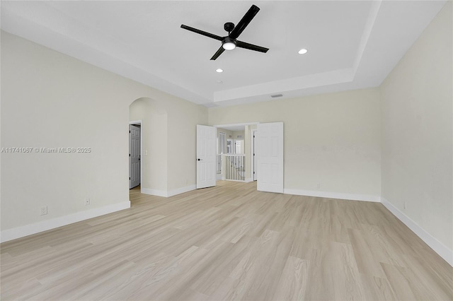 unfurnished bedroom with ceiling fan, light wood-type flooring, and a tray ceiling