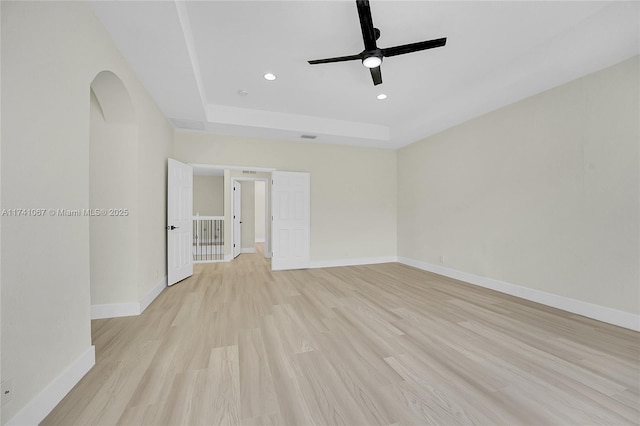 spare room featuring ceiling fan, a tray ceiling, and light hardwood / wood-style flooring