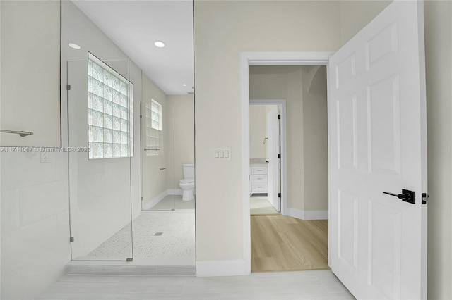 bathroom featuring hardwood / wood-style flooring, toilet, and a tile shower