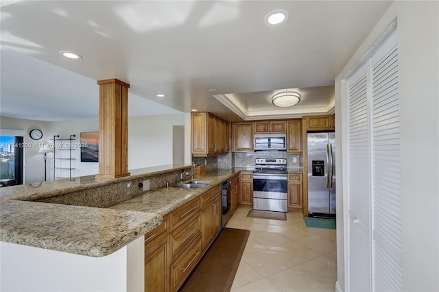 kitchen featuring sink, appliances with stainless steel finishes, a tray ceiling, kitchen peninsula, and light stone countertops