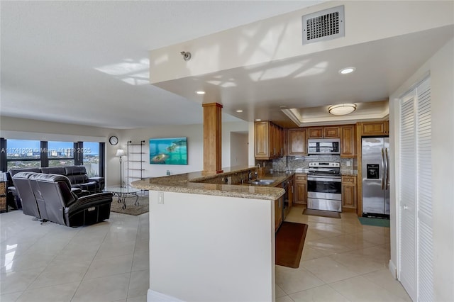 kitchen with a raised ceiling, light tile patterned flooring, appliances with stainless steel finishes, and kitchen peninsula