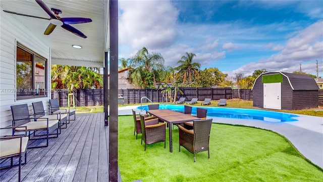 view of pool with a shed, a wooden deck, a lawn, and ceiling fan