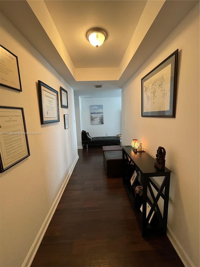 hallway with dark wood-type flooring and a raised ceiling