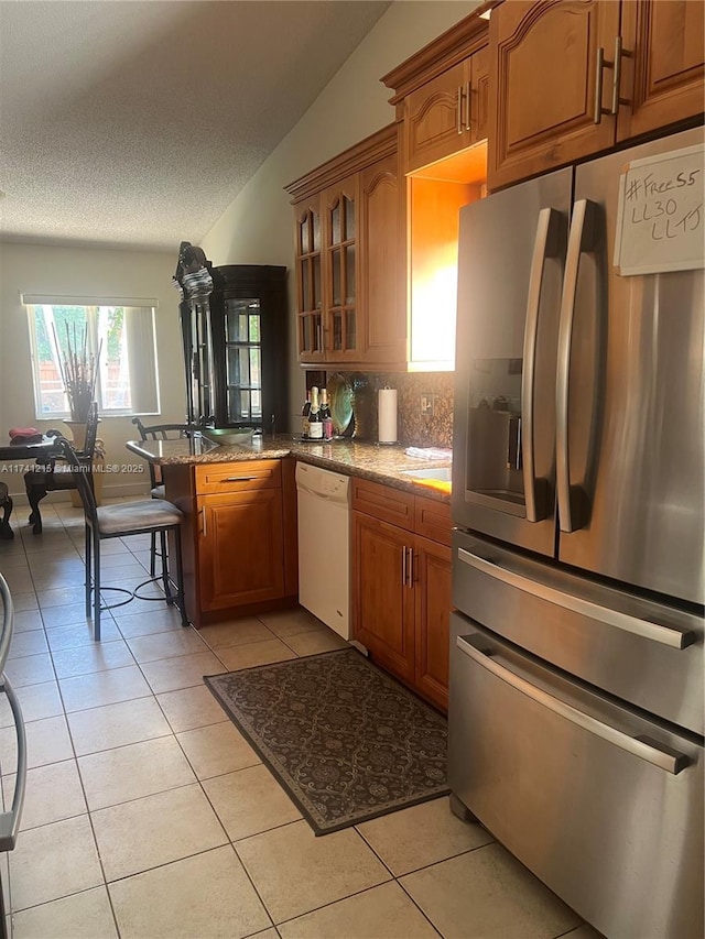 kitchen with a breakfast bar, dishwasher, stainless steel fridge, light tile patterned floors, and kitchen peninsula