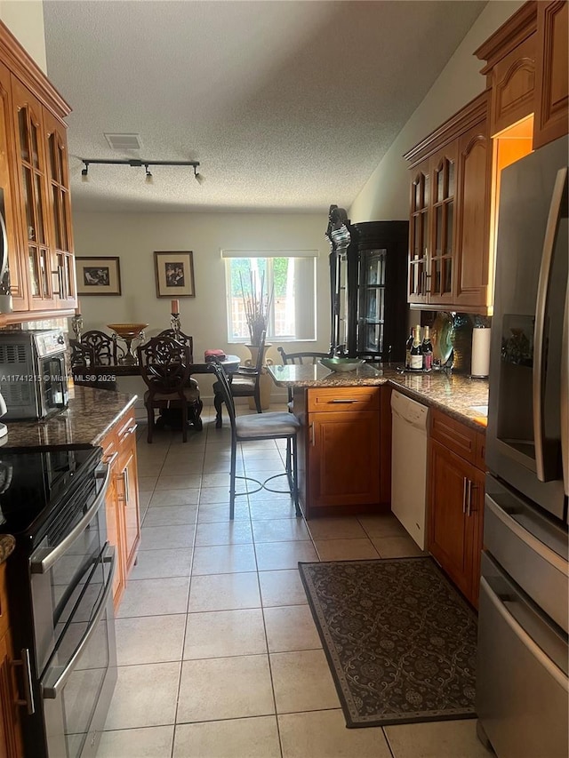 kitchen featuring tasteful backsplash, a textured ceiling, light tile patterned floors, appliances with stainless steel finishes, and dark stone counters