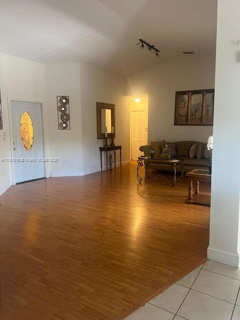 living room with rail lighting, vaulted ceiling, and light hardwood / wood-style floors