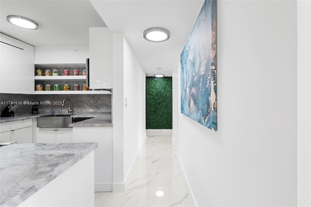 interior space with tasteful backsplash, baseboards, a sink, marble finish floor, and indoor wet bar