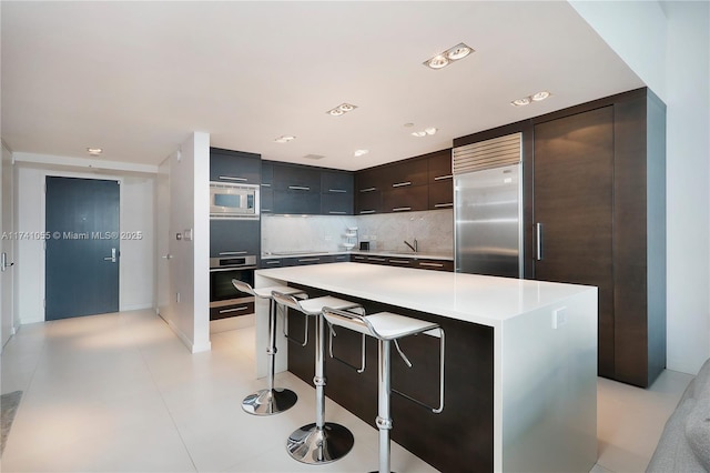 kitchen with tasteful backsplash, built in appliances, a center island, and a breakfast bar area