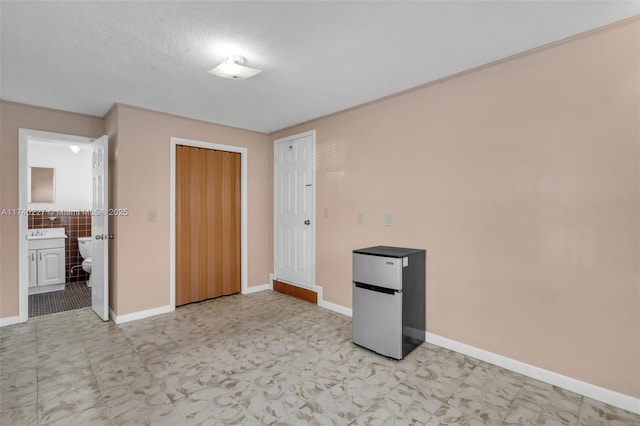 unfurnished bedroom with connected bathroom, stainless steel fridge, a closet, and a textured ceiling