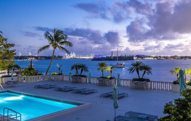 pool at dusk featuring a patio and a water view