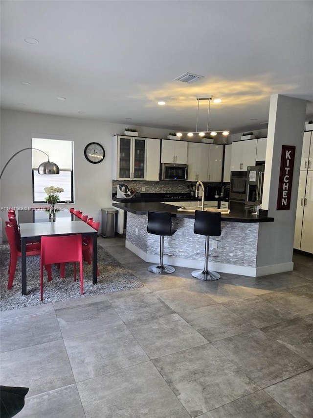 kitchen with tasteful backsplash, decorative light fixtures, appliances with stainless steel finishes, a kitchen breakfast bar, and white cabinets